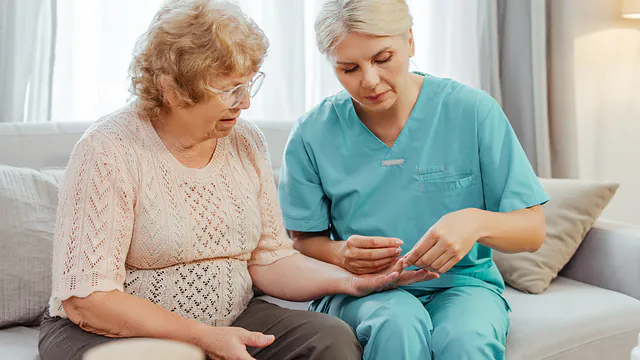 Pflegekraft gibt einer Seniorin auf dem Sofa ihre Tabletten