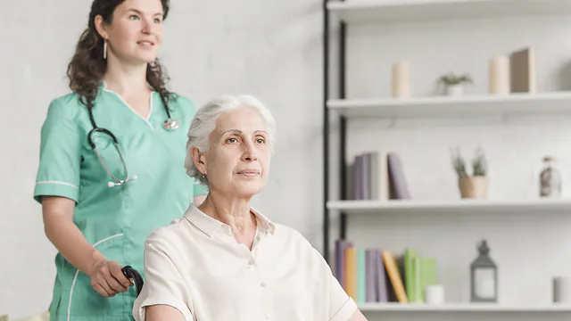 Pflegekraft begleitet eine Seniorin im Rollstuhl in ihrer Wohnung